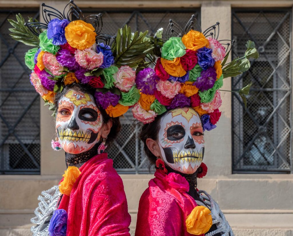 Dos personas con maquillaje de catrina y coronas de flores en Día de Muertos