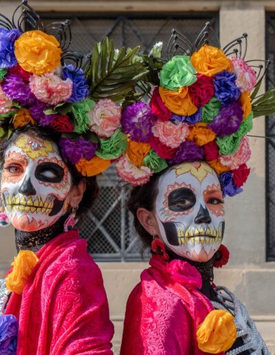 Dos personas con maquillaje de catrina y coronas de flores en Día de Muertos