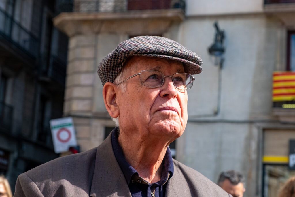 Hombre mayor con gorra y gafas en una calle con banderas