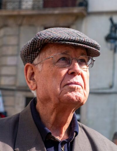 Hombre mayor con gorra y gafas en una calle con banderas