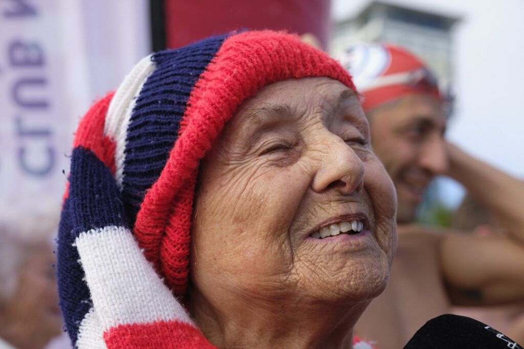 Mujer mayor con gorro de lana sonriendo en un evento al aire libre