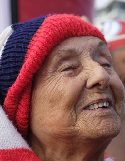 Mujer mayor con gorro de lana sonriendo en un evento al aire libre