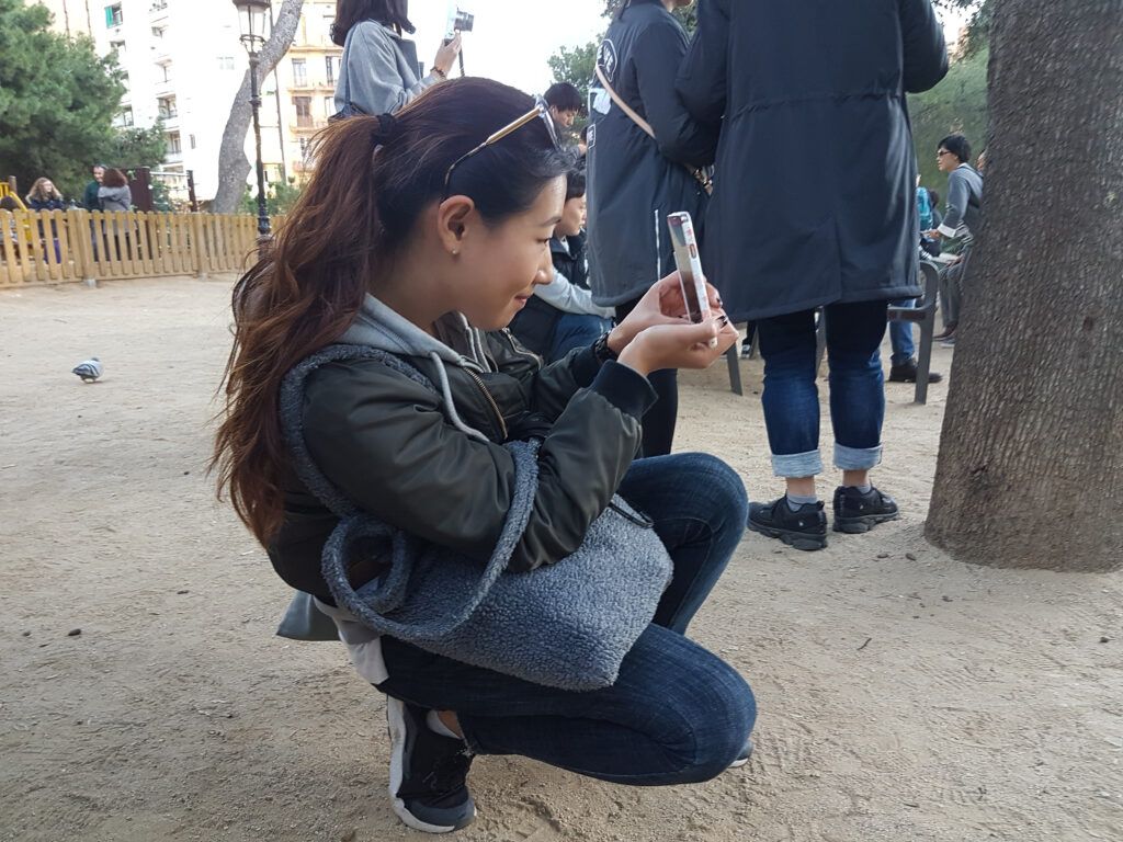Niña agachada tomando una foto con el móvil en un parque
