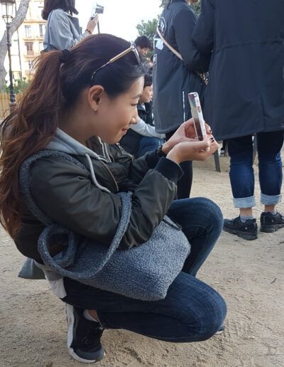 Niña agachada tomando una foto con el móvil en un parque