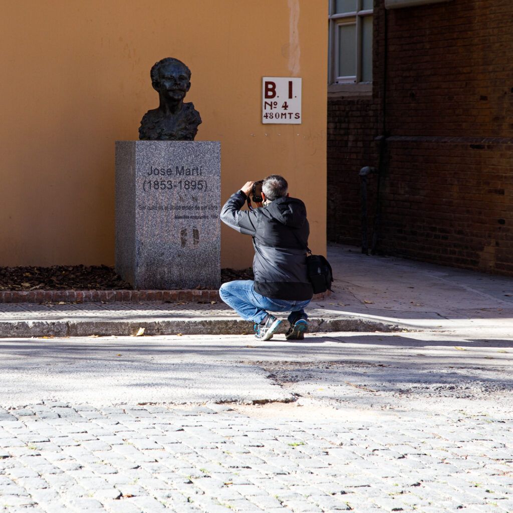 Persona agachada fotografiando cerca de una escultura