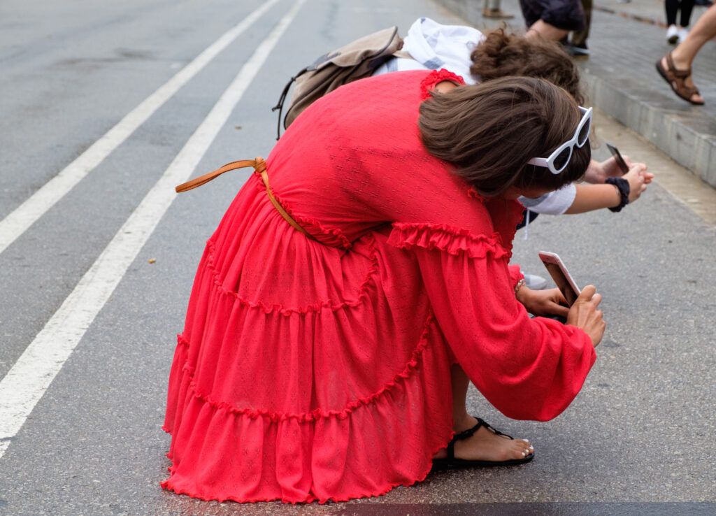 Mujer con vestido rojo agachada fotografiando en la calle