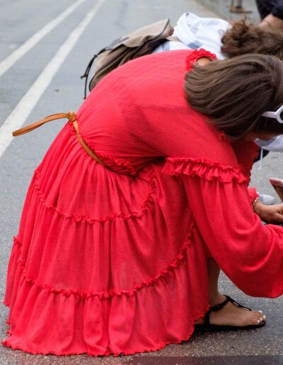 Mujer con vestido rojo agachada fotografiando en la calle