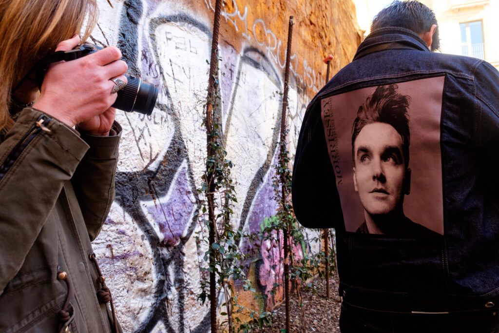 Persona fotografiando junto a un muro con un cartel y grafiti