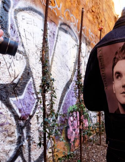 Persona fotografiando junto a un muro con un cartel y grafiti