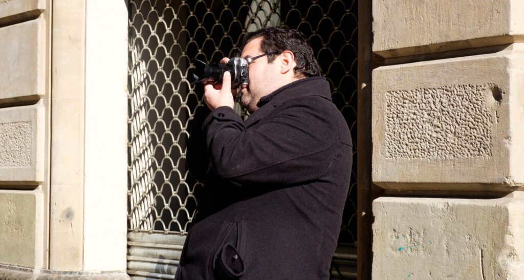 Hombre con abrigo fotografiando con su cámara junto a un edificio