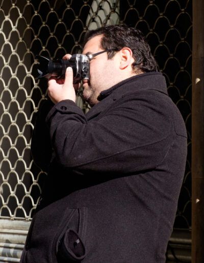 Hombre con abrigo fotografiando con su cámara junto a un edificio