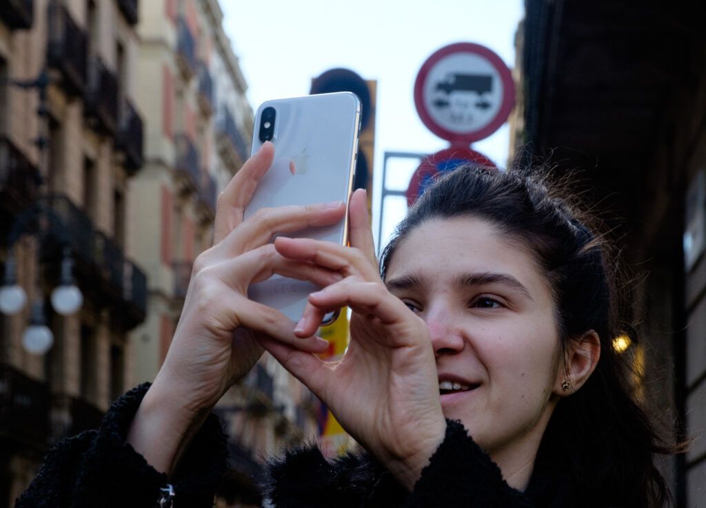 Mujer joven tomando una foto con el teléfono móvil en la calle