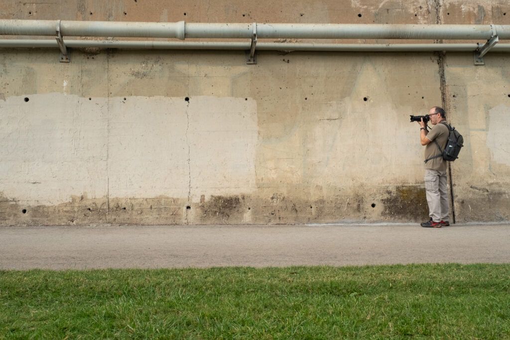 Fotógrafo de pequeño tamaño disparando ante un gran muro de hormigón