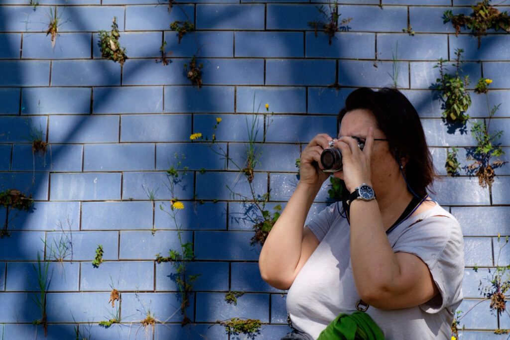 Mujer fotografiando con su cámara ante un muro de azulejos azules