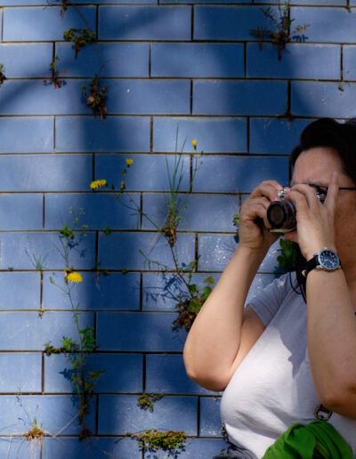 Mujer fotografiando con su cámara ante un muro de azulejos azules