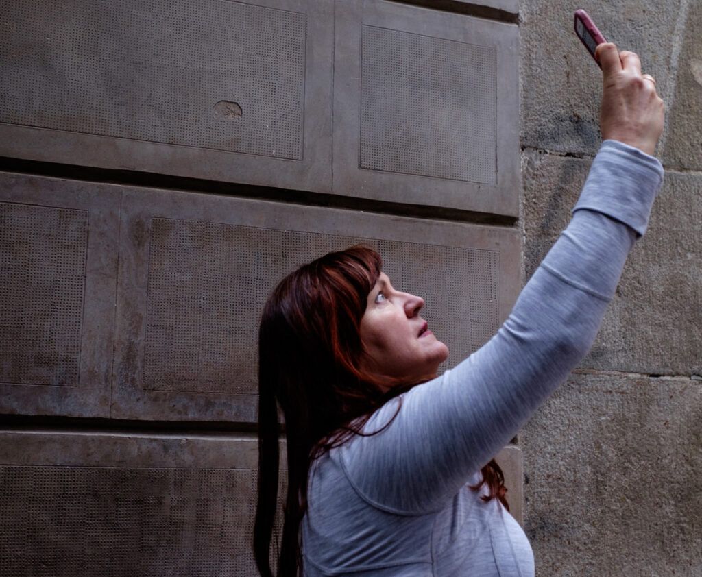 Mujer con el brazo en alto fotografiando con el móvil junto a un muro