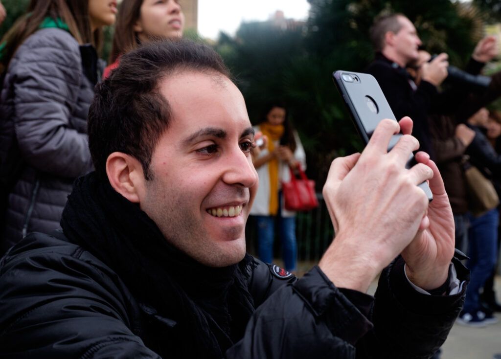 Joven sonriente fotografiando con su teléfono móvil entre la multitud