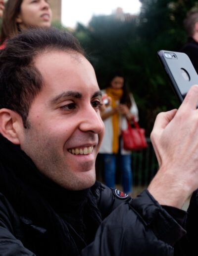 Joven sonriente fotografiando con su teléfono móvil entre la multitud