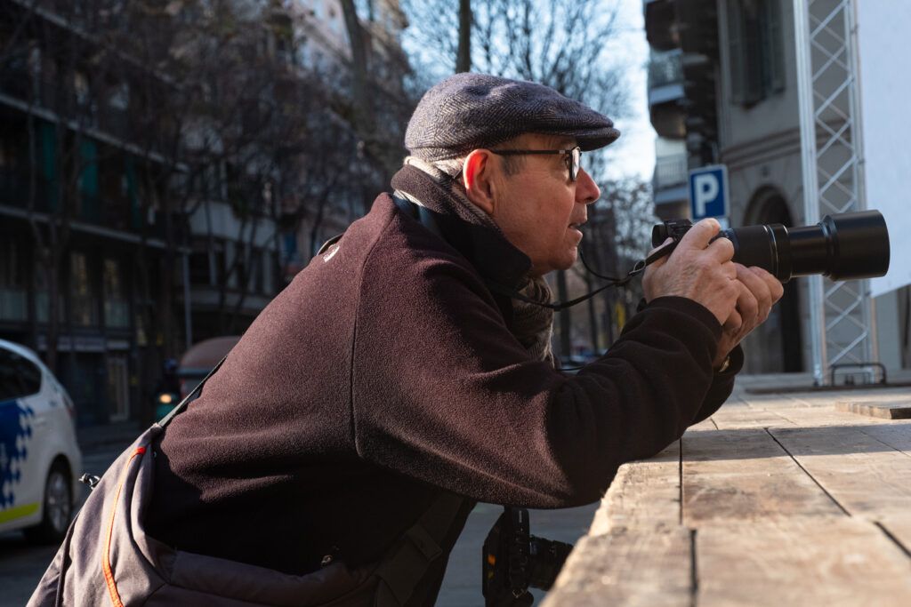 Hombre con gorra fotografiando con un teleobjetivo en la calle