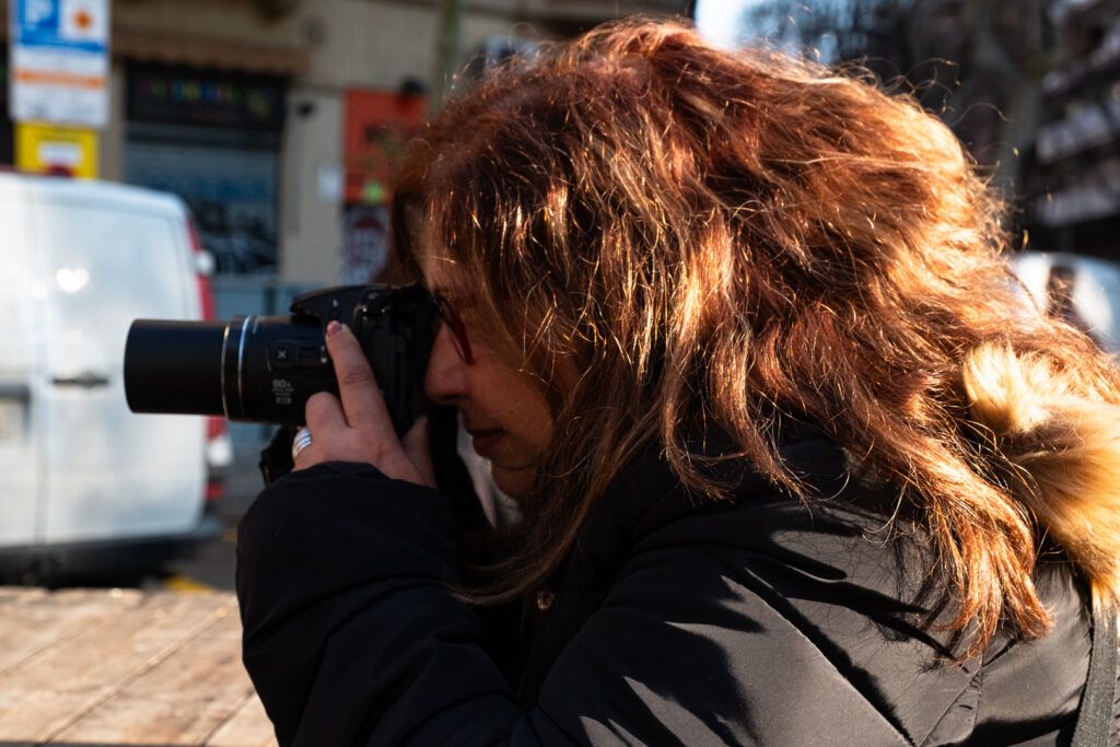 Mujer de cabello rojizo fotografiando con una cámara réflex en la calle