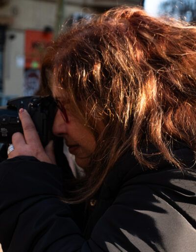 Mujer de cabello rojizo fotografiando con una cámara réflex en la calle