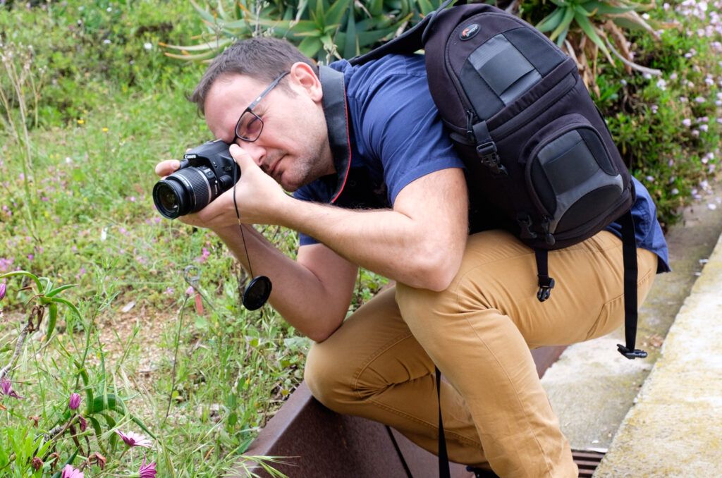 Fotógrafo con mochila agachado disparando junto a la vegetación