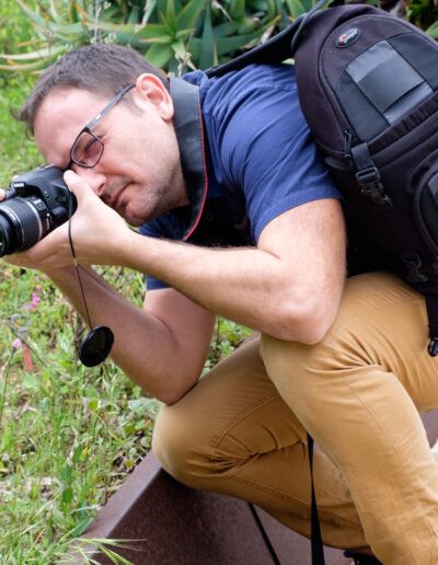 Fotógrafo con mochila agachado disparando junto a la vegetación
