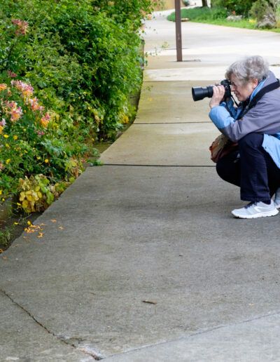 Fotógrafo agachado disparando junto a unos setos en la calle