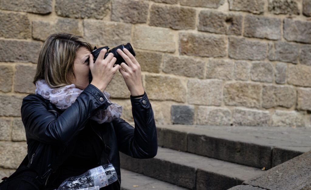 Mujer con pañuelo fotografiando con su cámara ante un muro de piedra
