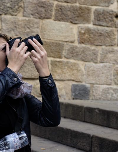 Mujer con pañuelo fotografiando con su cámara ante un muro de piedra