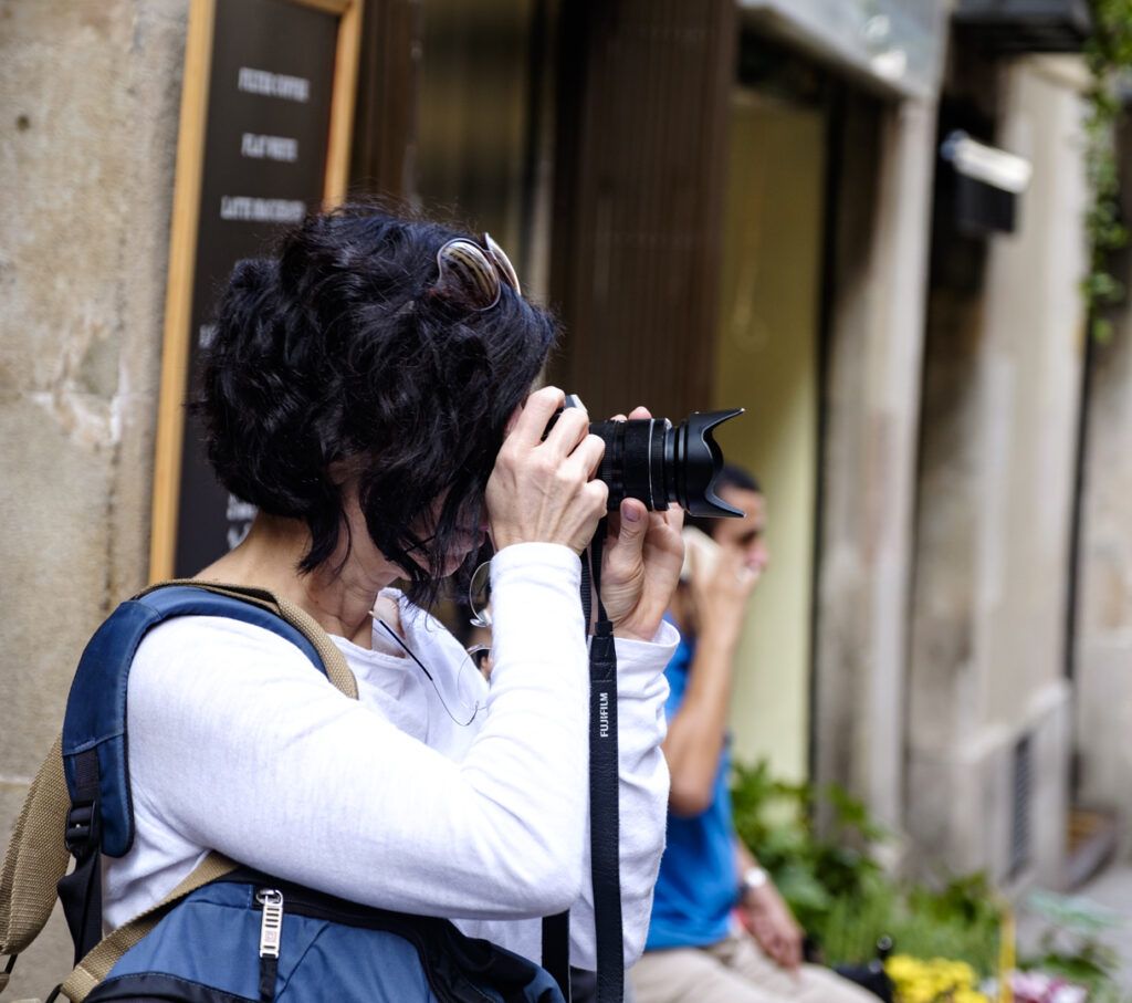 Mujer con mochila fotografiando con su cámara en una calle de Barcelona
