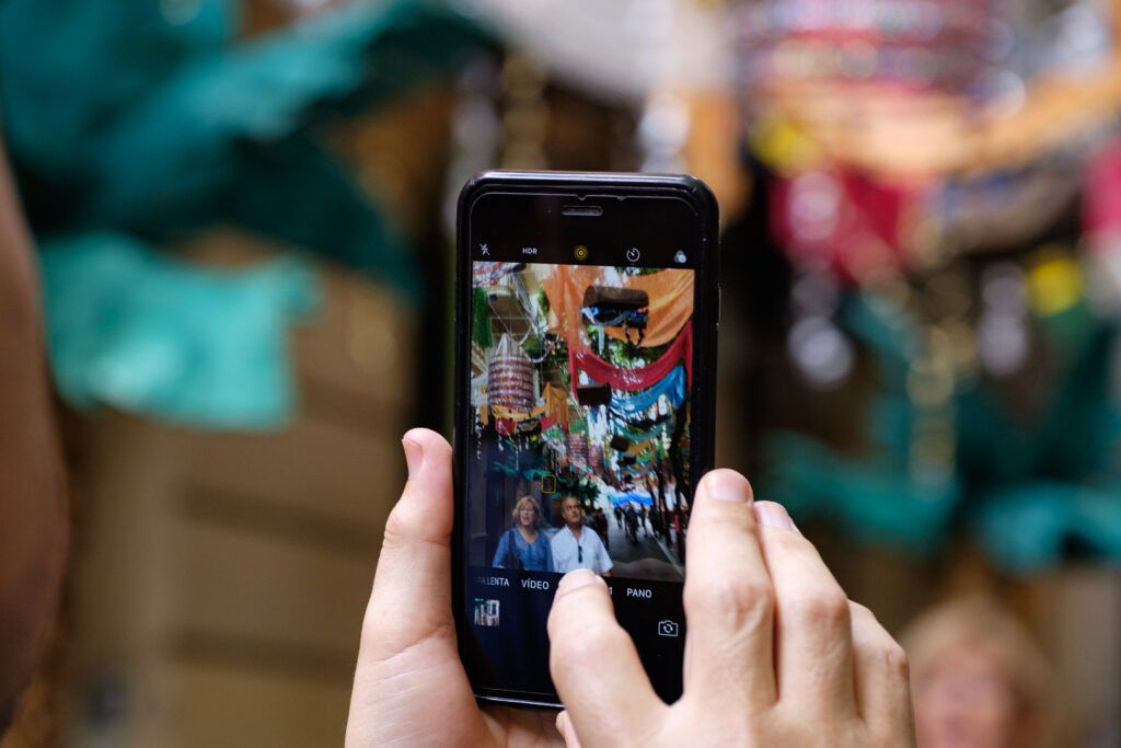 Manos sosteniendo un teléfono móvil que fotografía un colorido puesto de mercado