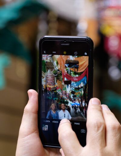 Manos sosteniendo un teléfono móvil que fotografía un colorido puesto de mercado