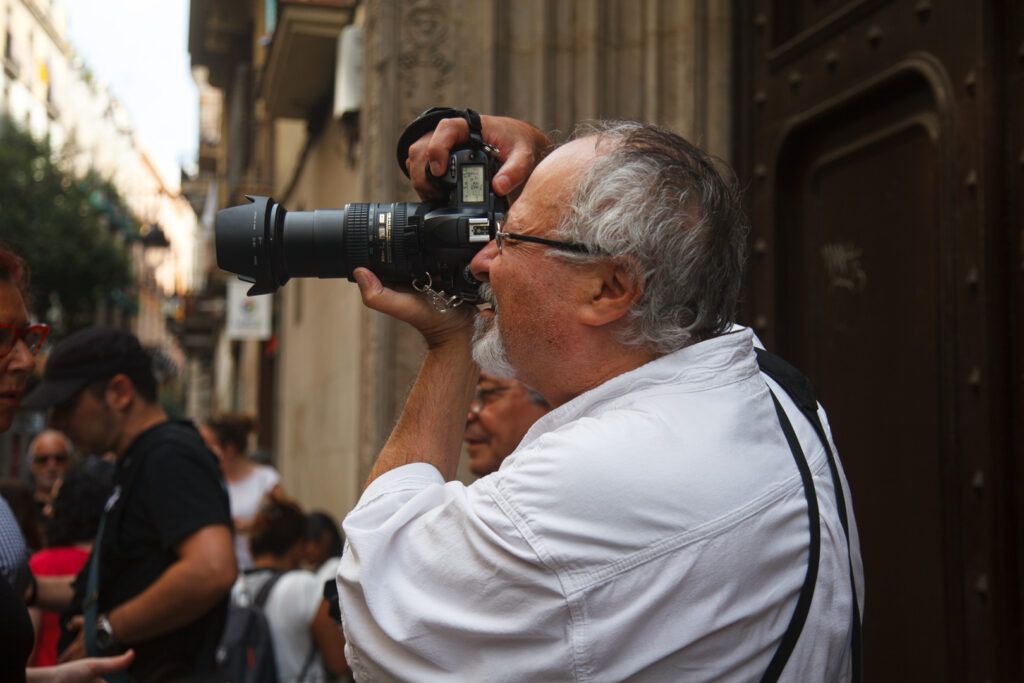 Hombre mayor con gafas fotografiando con una cámara réflex entre la gente