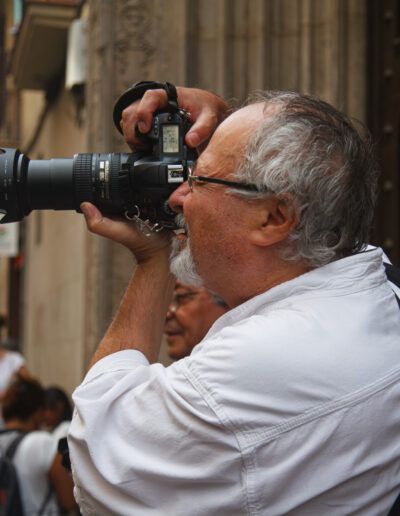 Hombre mayor con gafas fotografiando con una cámara réflex entre la gente