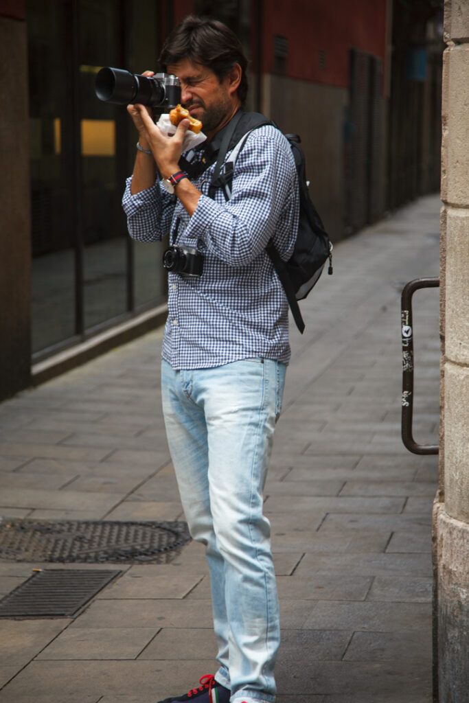 Fotógrafo con vaqueros disparando con su cámara en una calle de Barcelona