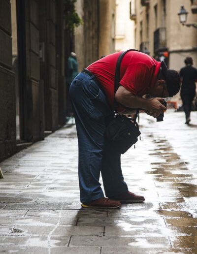 Fotógrafo con sudadera roja agachado disparando en una calle mojada de Barcelona