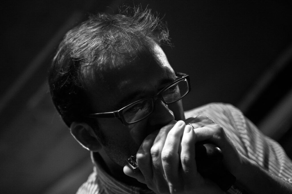 Armonicista con gafas tocando la armónica en primer plano, fotografía en blanco y negro