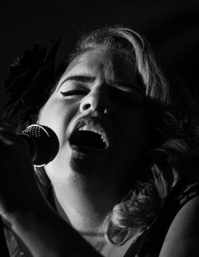 Primer plano de cantante femenina con flor en el pelo cantando ante el micrófono, blanco y negro