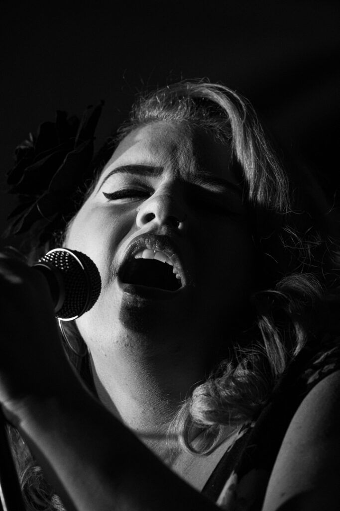 Primer plano de cantante femenina con flor en el pelo cantando ante el micrófono, blanco y negro