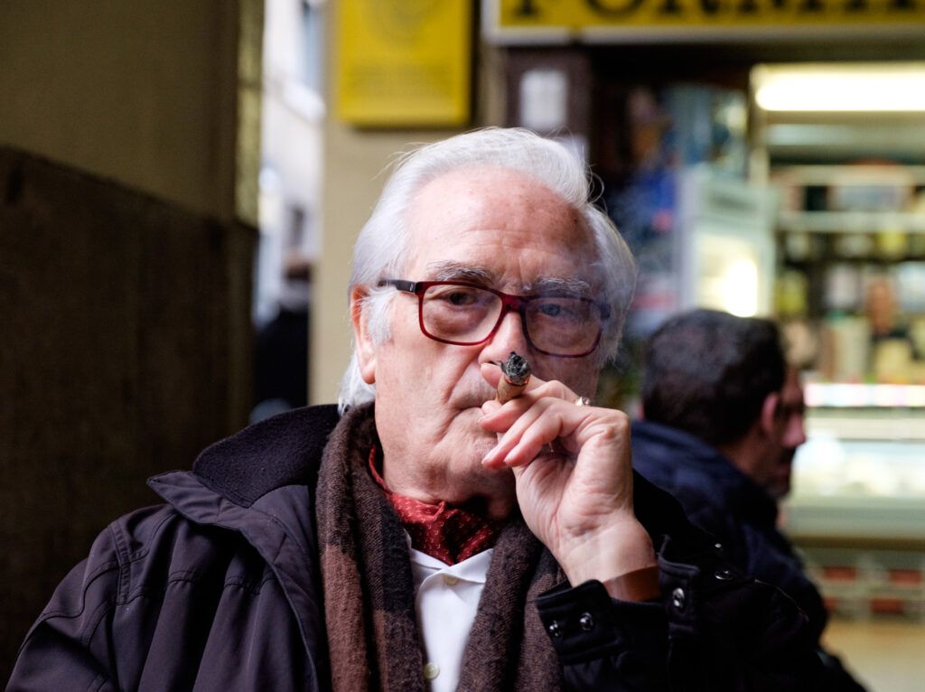 Retrato de un hombre mayor con gafas fumando un puro en un bar