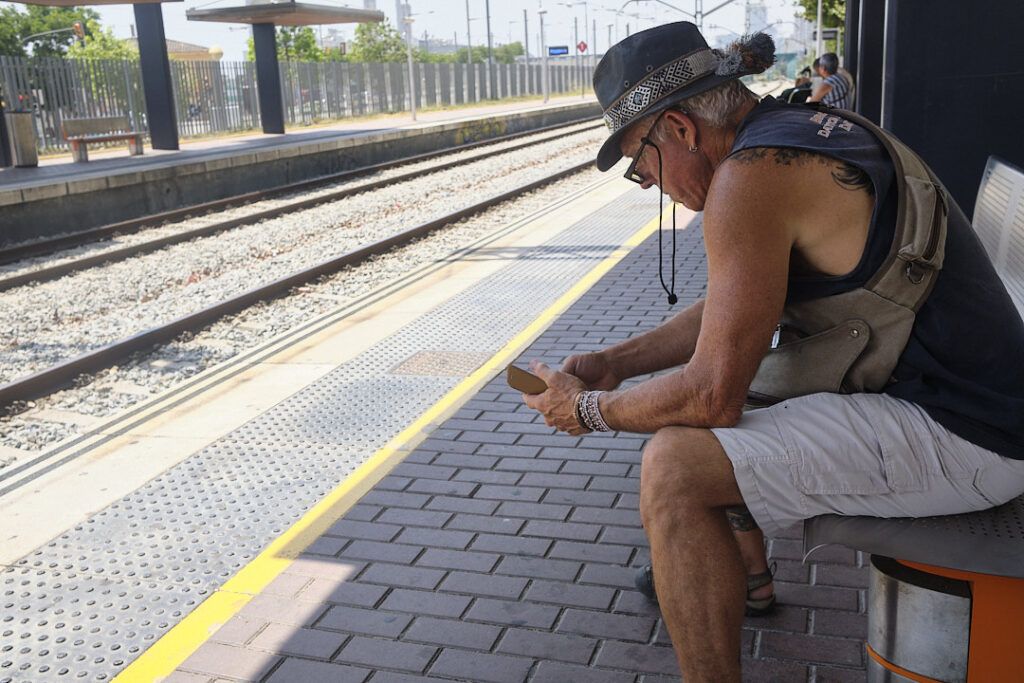 Hombre con sombrero mirando el móvil sentado en el andén de una estación