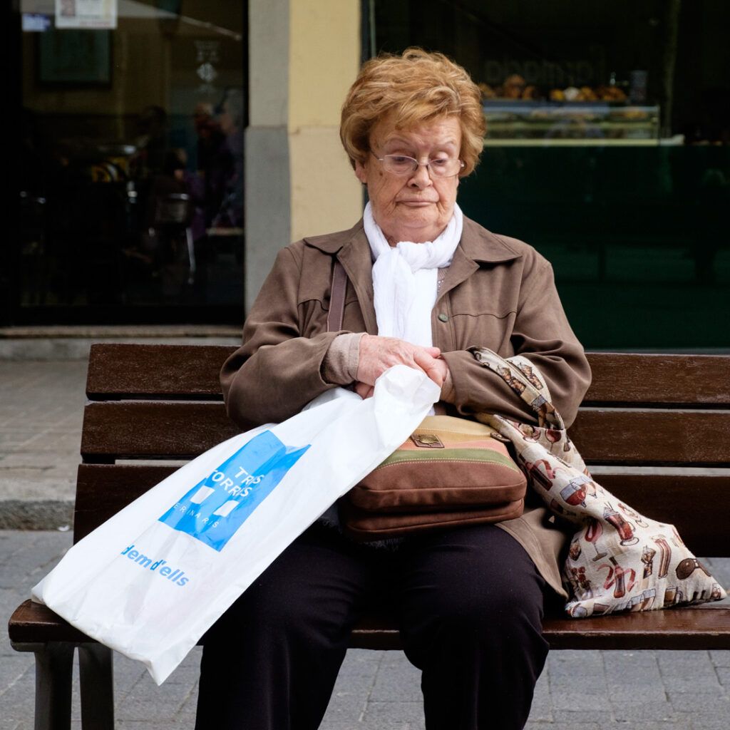 Mujer mayor sentada en un banco con una bolsa de plástico