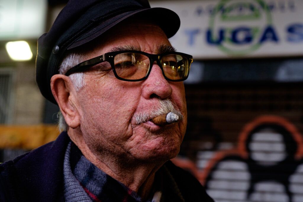 Retrato de un hombre con gorra y gafas fumando un puro