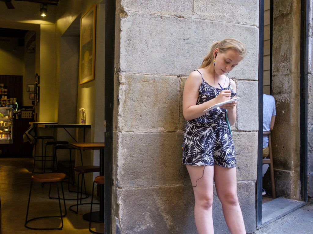 Mujer joven apoyada en una pared de piedra mirando el móvil