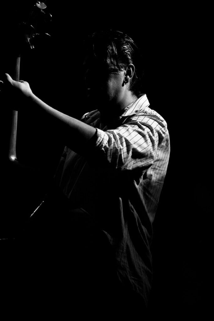 Contrabajista de perfil tocando el contrabajo en penumbra, fotografía en blanco y negro