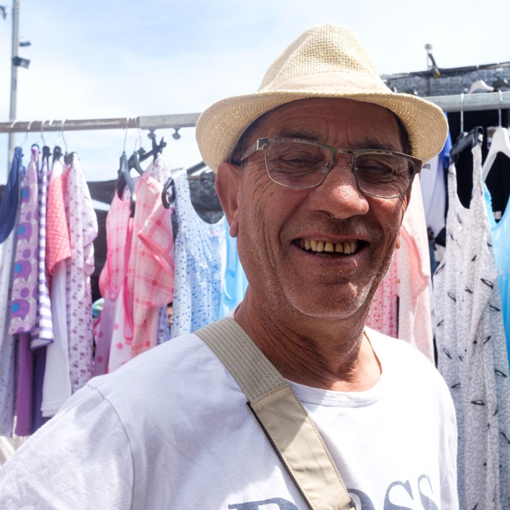 Retrato de un hombre sonriente con sombrero y gafas en un mercadillo