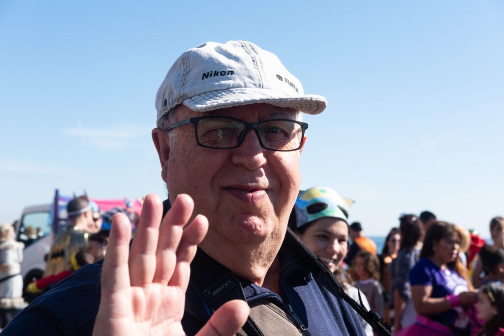 Hombre mayor con gorra saludando en una fiesta junto a la playa