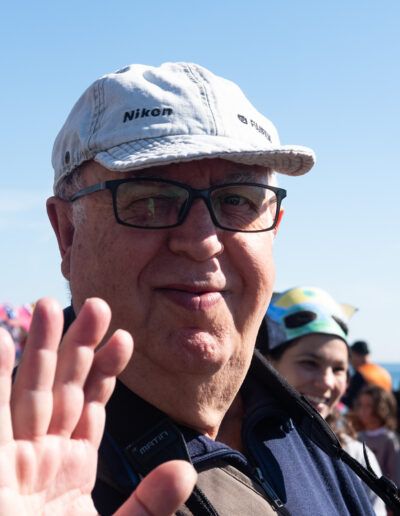 Hombre mayor con gorra saludando en una fiesta junto a la playa