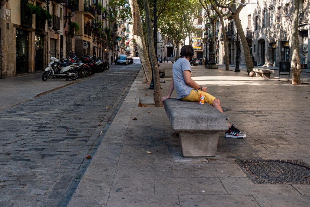 Persona sentada en un banco de piedra escuchando música en una calle arbolada